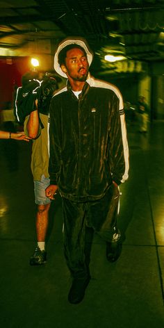 a man in a hat and jacket walking down the street with a camera on his shoulder