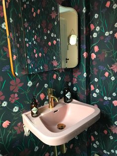 a pink sink sitting under a bathroom mirror next to a wall mounted faucet