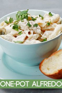 a blue bowl filled with pasta and bread on top of a plate next to a piece of bread