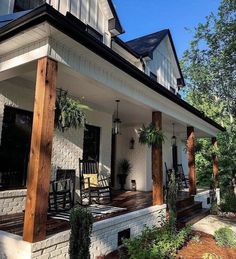 a porch with rocking chairs and plants on the front steps, next to a white brick house