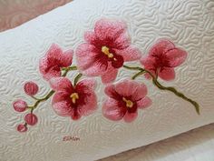 pink flowers are embroidered onto the back of a pillow cover that is on a bed