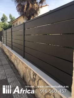 a fence that is next to a stone wall and palm trees on the side of it