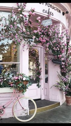 a pink bicycle is parked in front of a store with flowers growing out of the windows