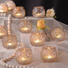 a table topped with lots of lit candles next to white beads and flowers in vases