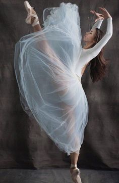 a woman in white dress and ballet shoes doing a dance move with her arms stretched out