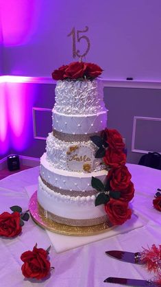 a three tiered wedding cake with red roses on the table