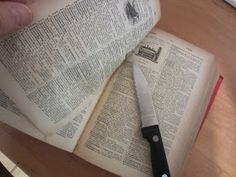 a person is holding an open book with a knife on top of it next to some books