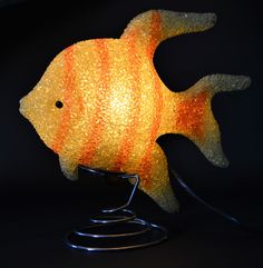 a yellow fish lamp sitting on top of a metal stand next to a black wall