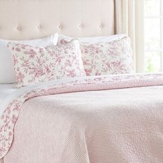 a bed with pink and white comforters in front of a window