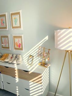 a white dresser topped with lots of shoes next to a lamp and pictures on the wall