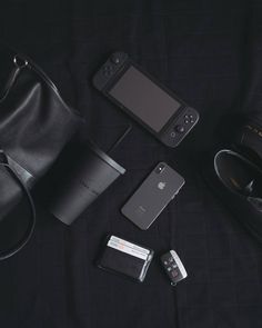 an assortment of electronics and accessories laid out on a black cloth with a handbag