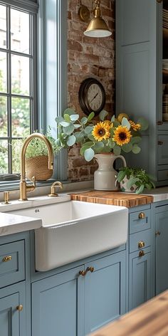 a kitchen with blue cabinets and sunflowers on the counter top in front of a brick wall