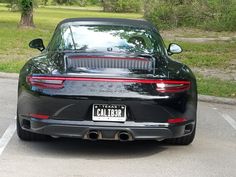 the back end of a black sports car parked in a parking lot next to trees