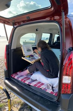 a woman sitting in the back of a red car looking at a book on her lap