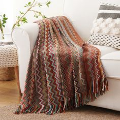 a white couch with a blanket on top of it next to a potted plant