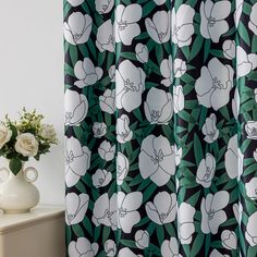 a white vase sitting next to a green and black shower curtain with flowers on it