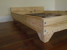 a wooden bed frame sitting on top of a hard wood floor next to a wall