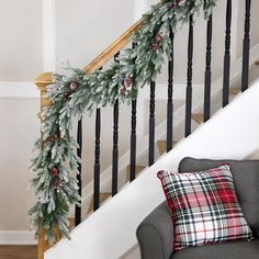 a christmas garland is hanging on the bannister next to a stair case with plaid pillows