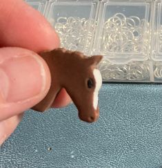 a small toy horse is being held in front of a plastic container with other items