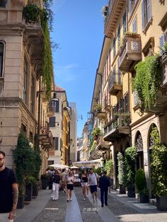 people are walking down the street in an old town with tall buildings and plants growing on the balconies