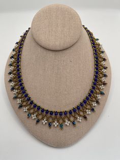 a necklace with blue and white beads on a mannequin head stand, wearing a beige dress