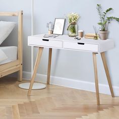 a white desk with two drawers and plants on it next to a bed in a room