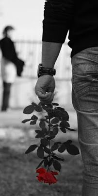 black and white photograph of a person holding a red rose in their hand with another person walking behind them