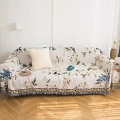 a white couch sitting on top of a hard wood floor next to a lamp and window