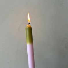 a pink and green candle sitting on top of a wooden table next to a white wall