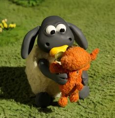 a stuffed animal is holding an orange teddy bear in its mouth while standing on the grass