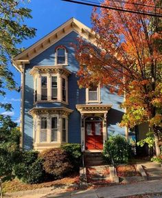 a blue two story house with red front door and trees in the fall colors around it