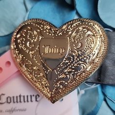 a gold heart shaped brooch sitting on top of a blue flowery background with the word couture written in it