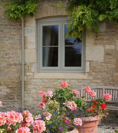 several potted flowers in front of a stone building with a bench next to it