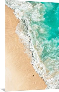 an aerial view of the ocean with two surfers in the water and one on the beach