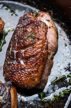 a piece of meat sitting on top of a pan covered in sauce and garnished with herbs