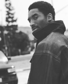 a man standing in front of a car wearing a scarf around his neck and looking off to the side