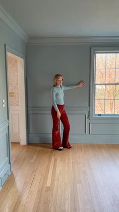 a woman standing in an empty room with her hand out and pointing at something on the wall