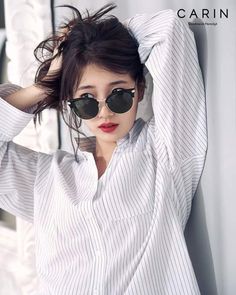 a woman wearing sunglasses leaning against a wall with her hand on her head and looking off to the side