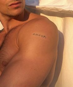 a man with no shirt on laying in bed and his arm tattoo reading amonna