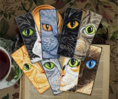 five bookmarks with cats painted on them next to a cup of tea