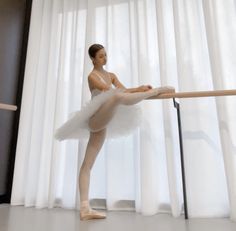 a young ballerina is practicing her moves on the ballet floor in front of white curtains