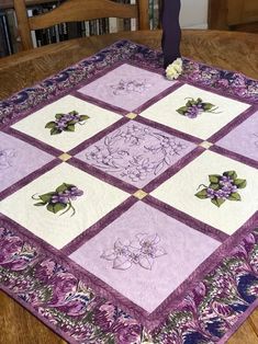 a purple and white quilted table topper on a wooden table with bookshelves in the background