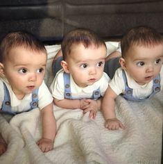 three babies are laying on a blanket and looking at the camera while wearing overalls