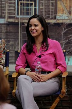 a woman sitting in a chair with a bottle of water on her lap while talking to someone