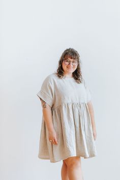 a woman standing in front of a white wall wearing glasses and a dress with short sleeves