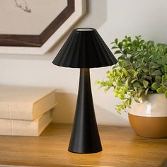 a black lamp sitting on top of a wooden table next to a potted plant