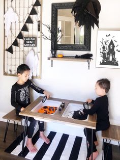 two young boys playing with halloween decorations on the table in front of a black and white striped rug