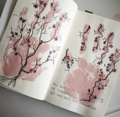 an open book with handprints on it and pink flowers in the middle, sitting on a table