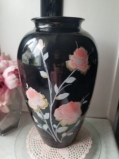 a black vase with pink flowers painted on it sitting on a table next to another vase