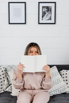 a woman sitting on a couch holding up a piece of paper in front of her face